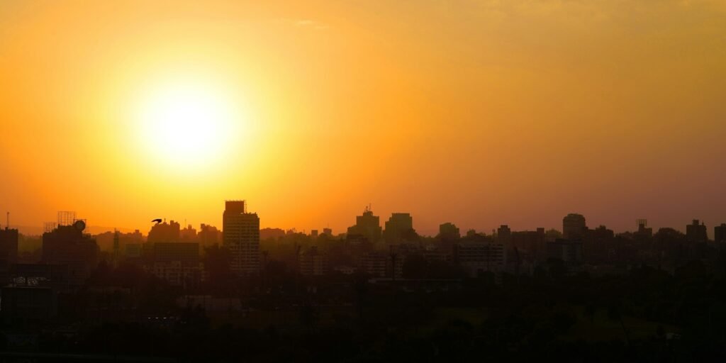 أفق مدينة عند الغروب، والشمس منخفضة في سماء ضبابية.